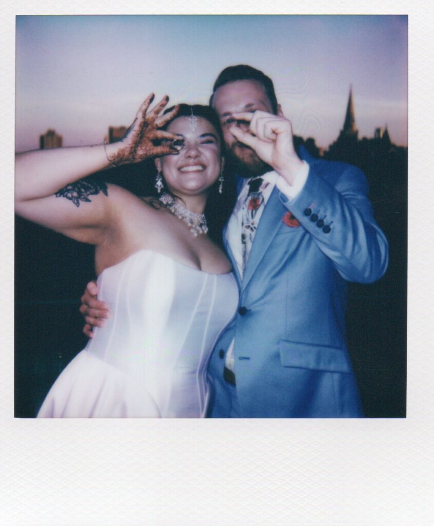 Polaroid of the bride and groom smiling while holding up their wedding rings during sunset on the rooftop at Solar Arts Building in Minneapolis.