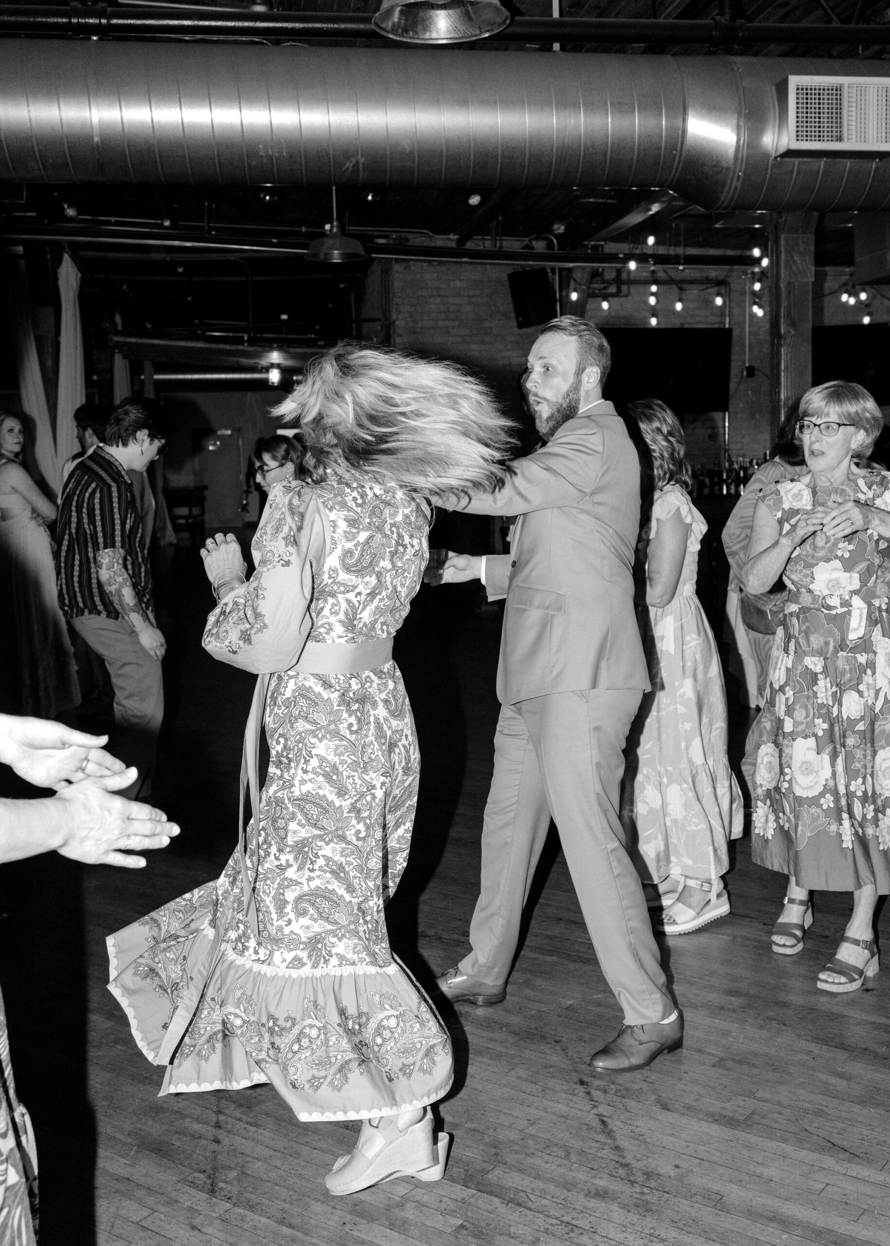 Black-and-white candid photo of wedding guests dancing during the reception celebration.