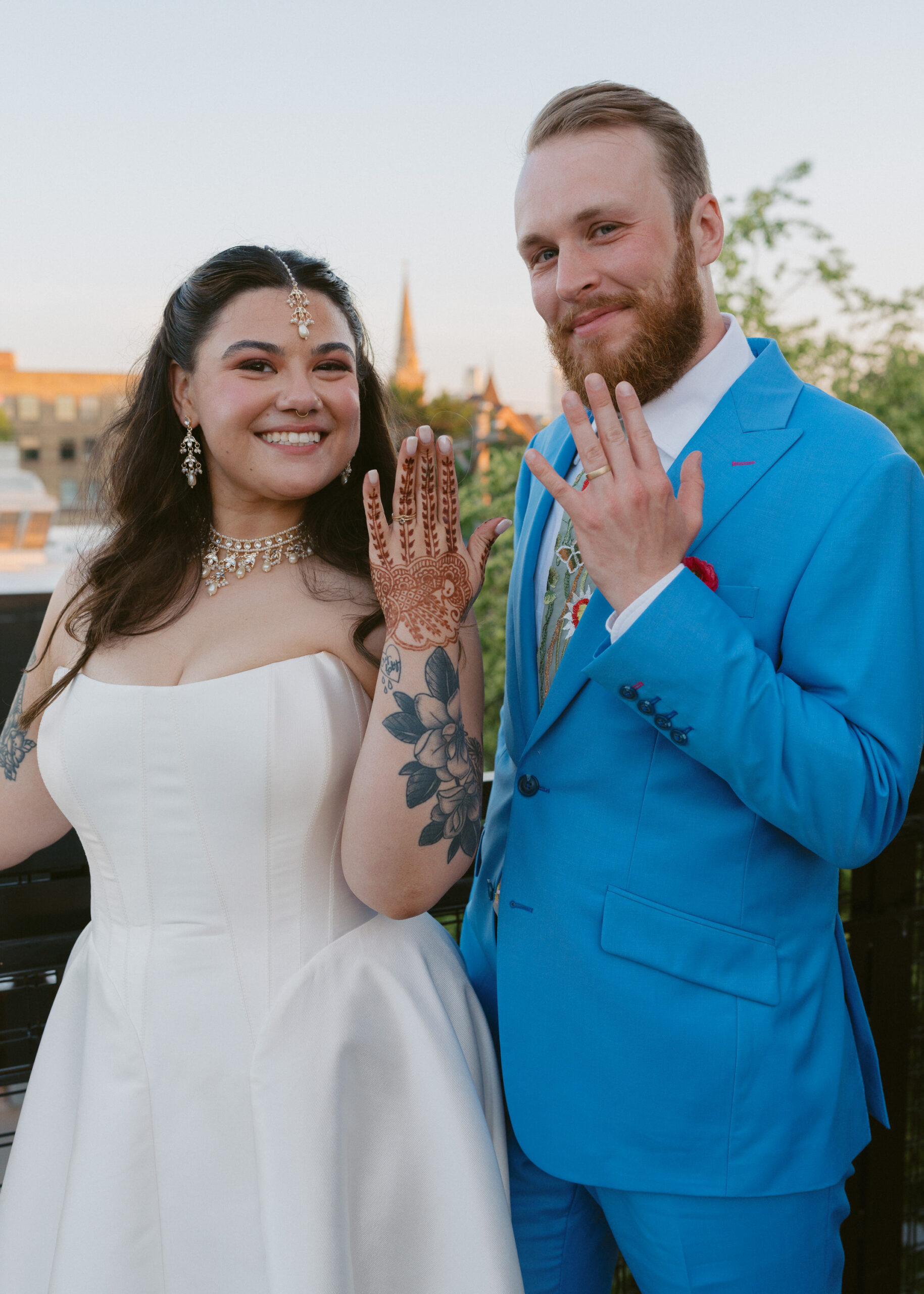 Bride and groom smile while showing their wedding rings during rooftop portraits at Solar Arts Building in Minneapolis.