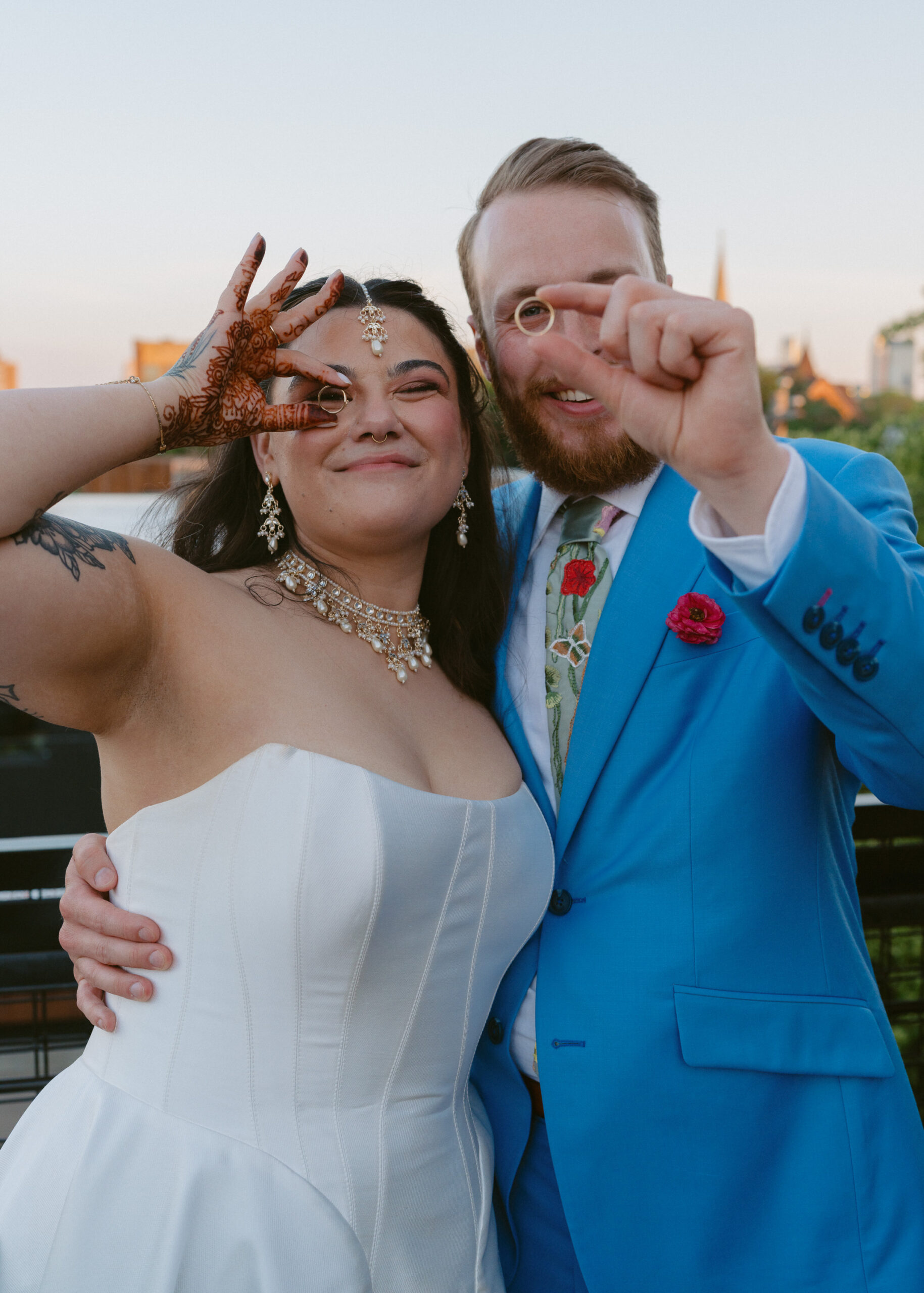 Bride and groom hold up their wedding rings during sunset portraits on the rooftop of Solar Arts Building in Minneapolis.