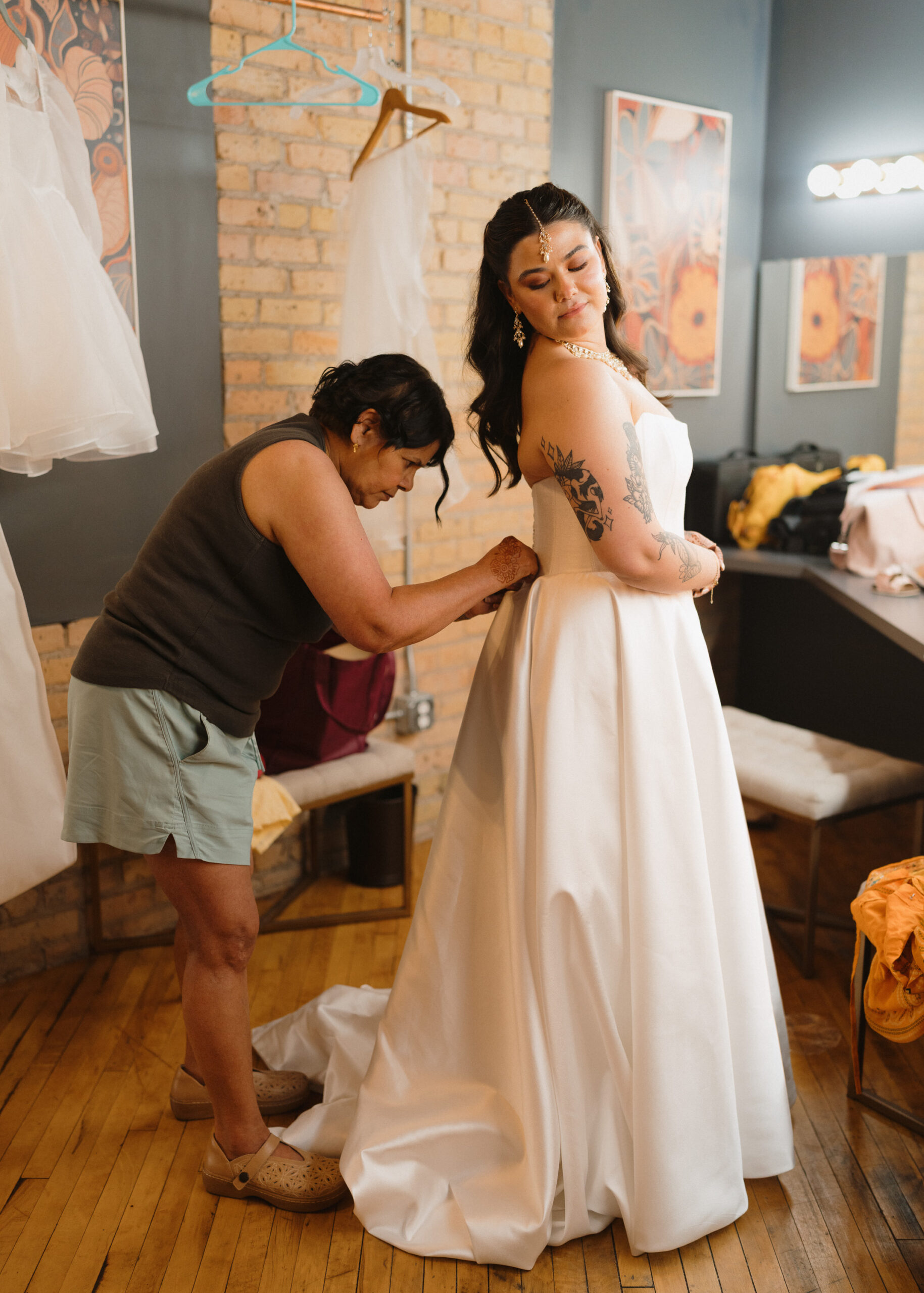 Bride smiles as her mother ties the back of her wedding dress during wedding morning preparations.