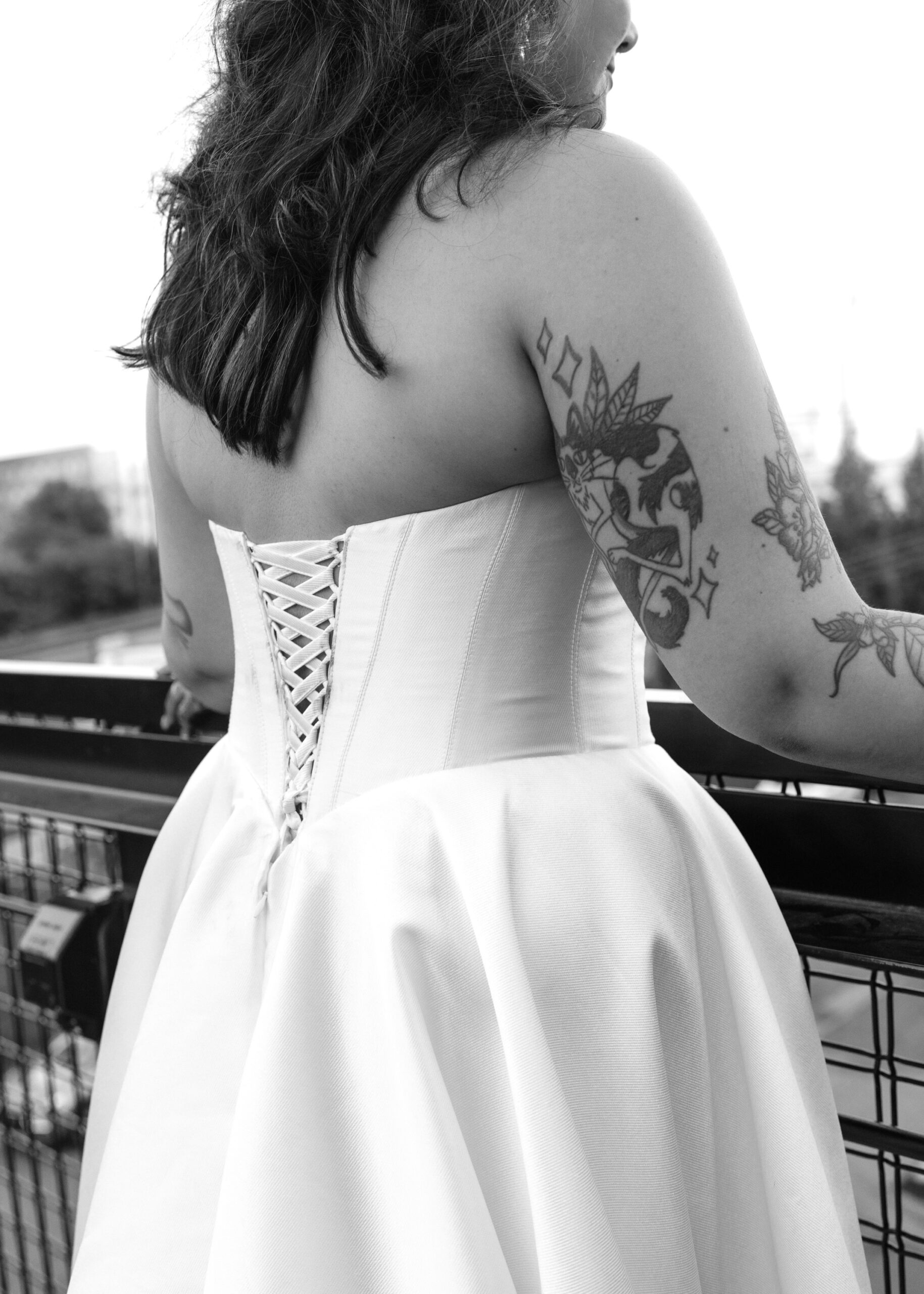 Black-and-white portrait of the bride overlooking Minneapolis, highlighting the lace-up back of her wedding dress and floral tattoos.