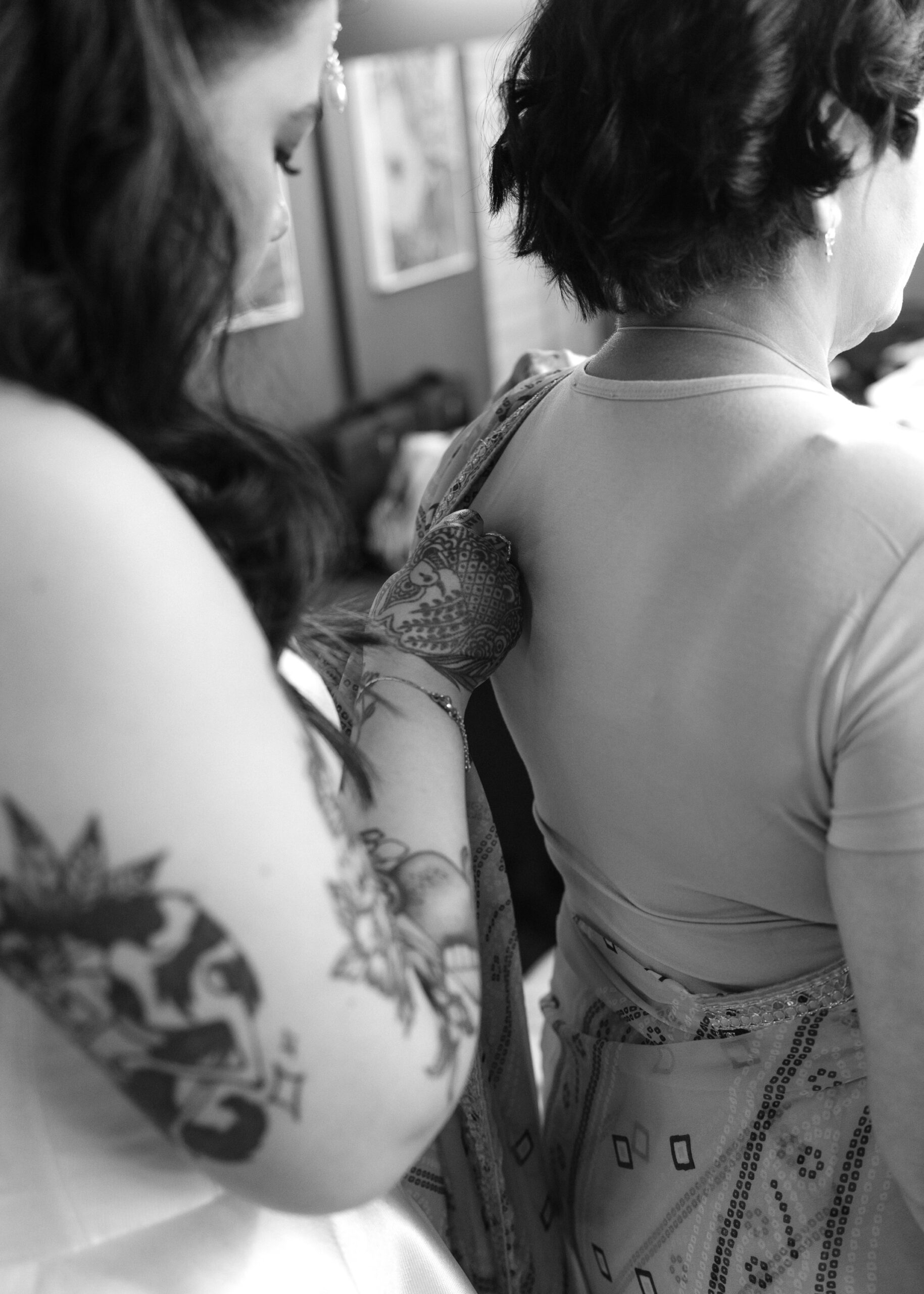 Bride fastens the back of her mother’s outfit during a quiet moment while getting ready for the wedding ceremony.