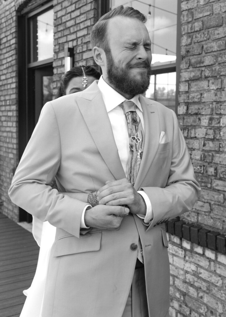 Groom closes his eyes and smiles as he waits for his bride to tap his shoulder during their first look