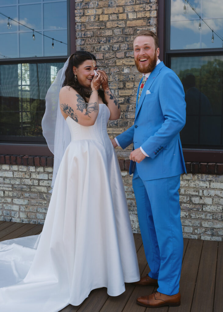 Bride and groom laugh and hold hands moments after seeing each other during their first look outside the Solar Arts Building.