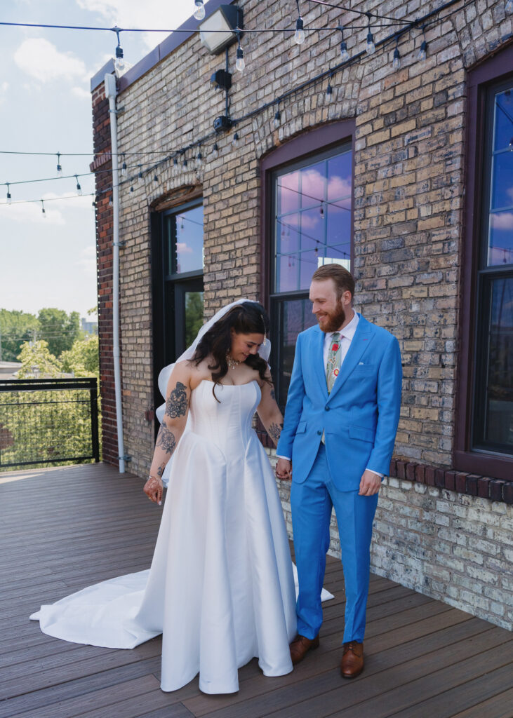 Bride and groom smile at each other while holding hands after their first look outside the Solar Arts Building in Minneapolis.