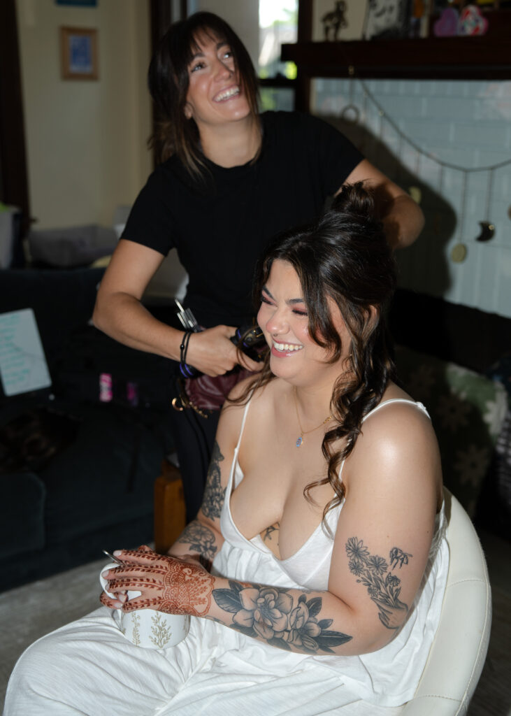 Bride smiles while having her hair styled during wedding morning preparations in Minneapolis.