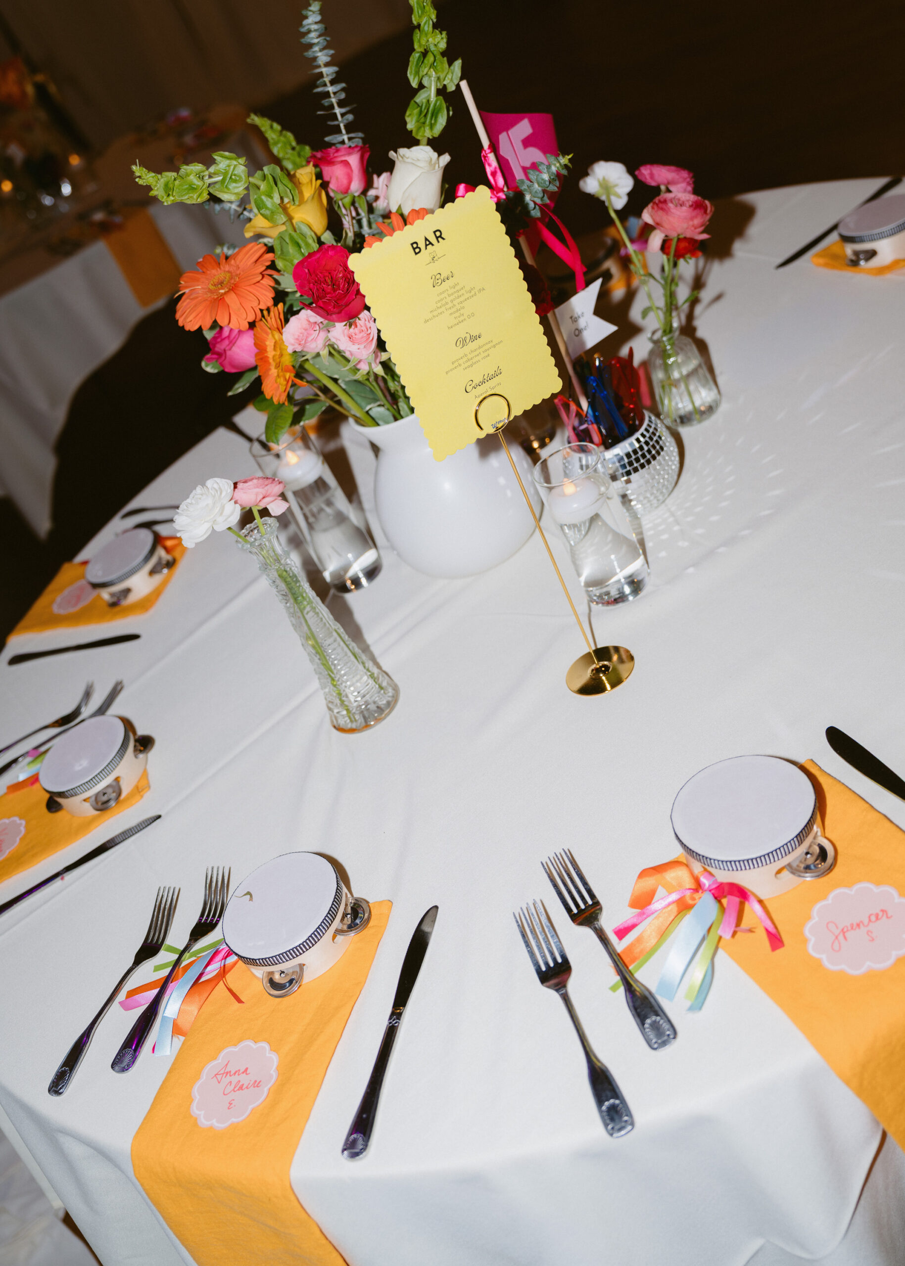 Colorful reception table centerpiece with bright flowers, a drink menu, and wedding table décor at the reception.