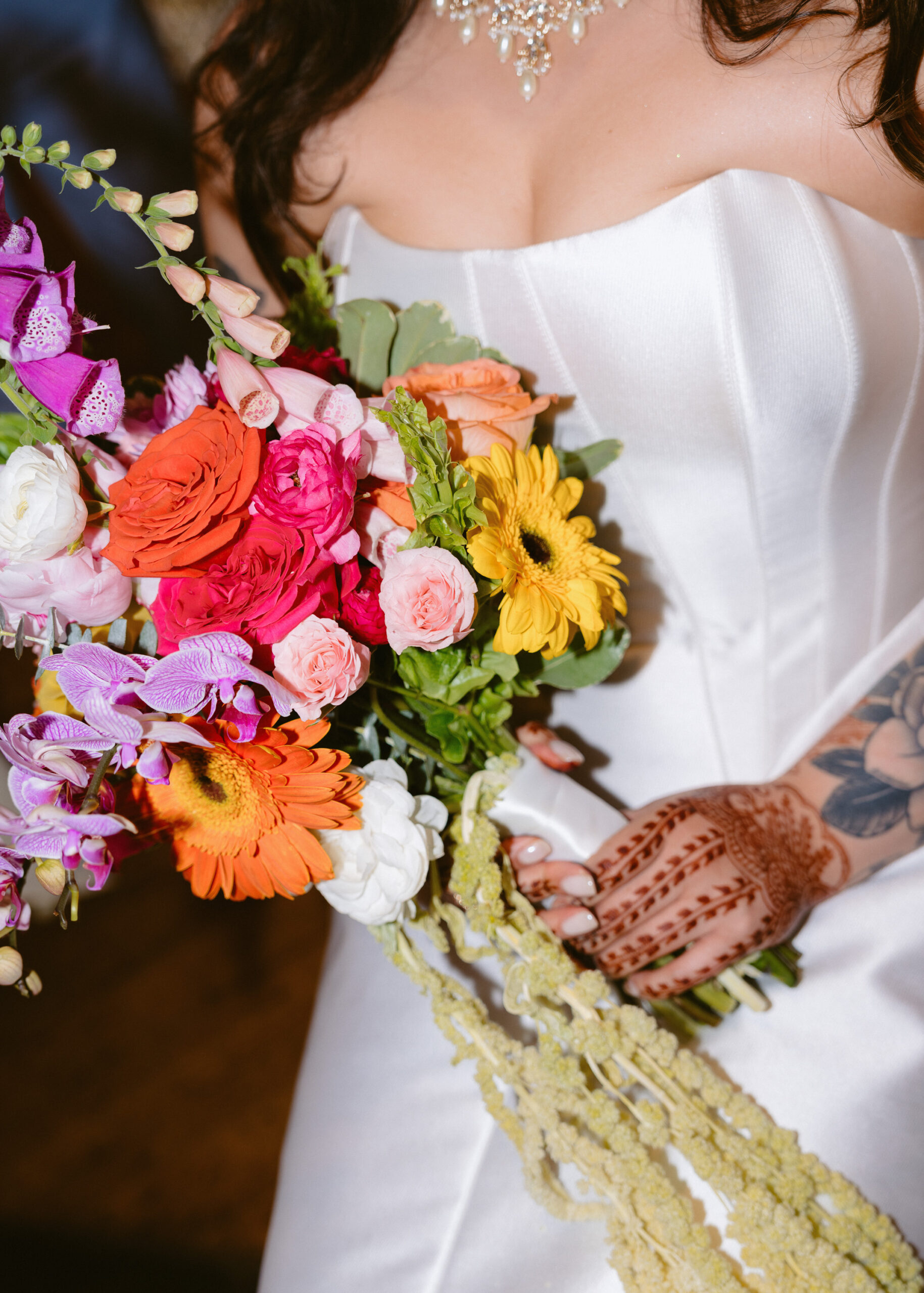 Bride holds her colorful wedding bouquet, showcasing vibrant flowers and intricate henna during the reception.