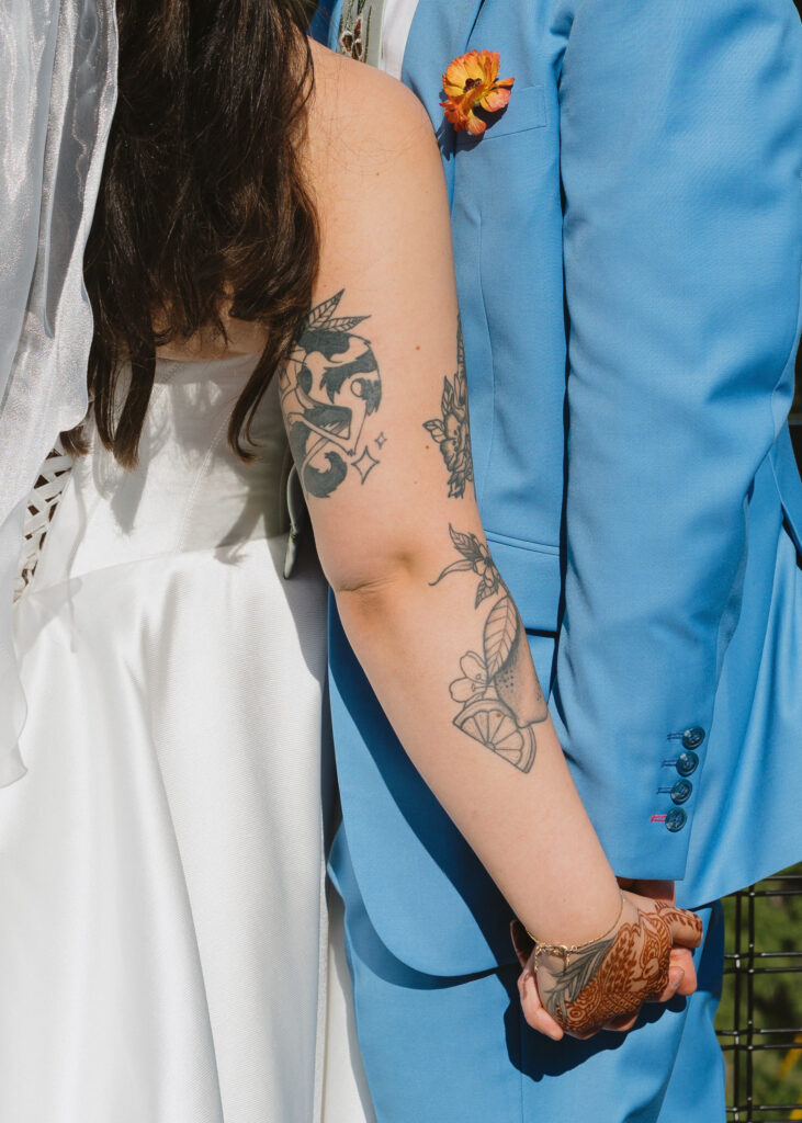Close-up of the bride and groom holding hands, highlighting the bride’s intricate henna and wedding dress.