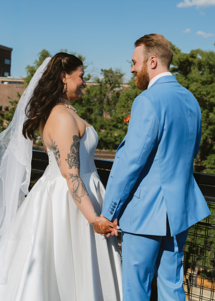 Bride and groom smile at each other while holding hands on a rooftop terrace after their wedding ceremony.