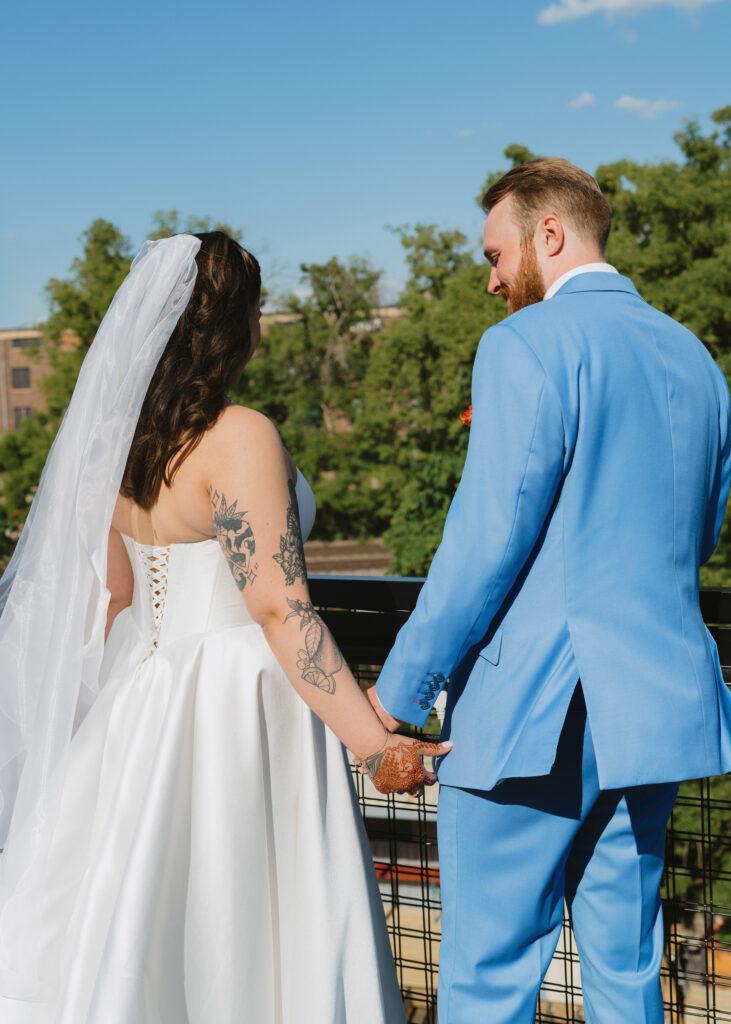 Bride and groom hold hands while admiring the view from a rooftop terrace after their wedding ceremony.