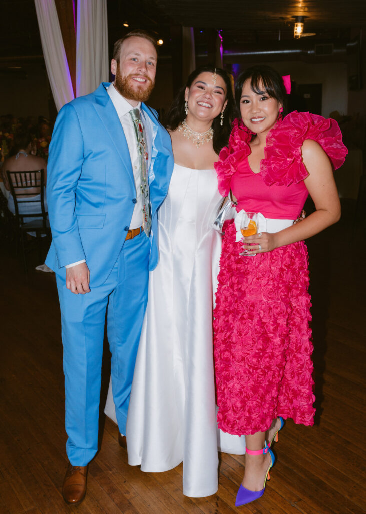 Bride and groom smile beside a wedding guest during the cocktail hour celebration.