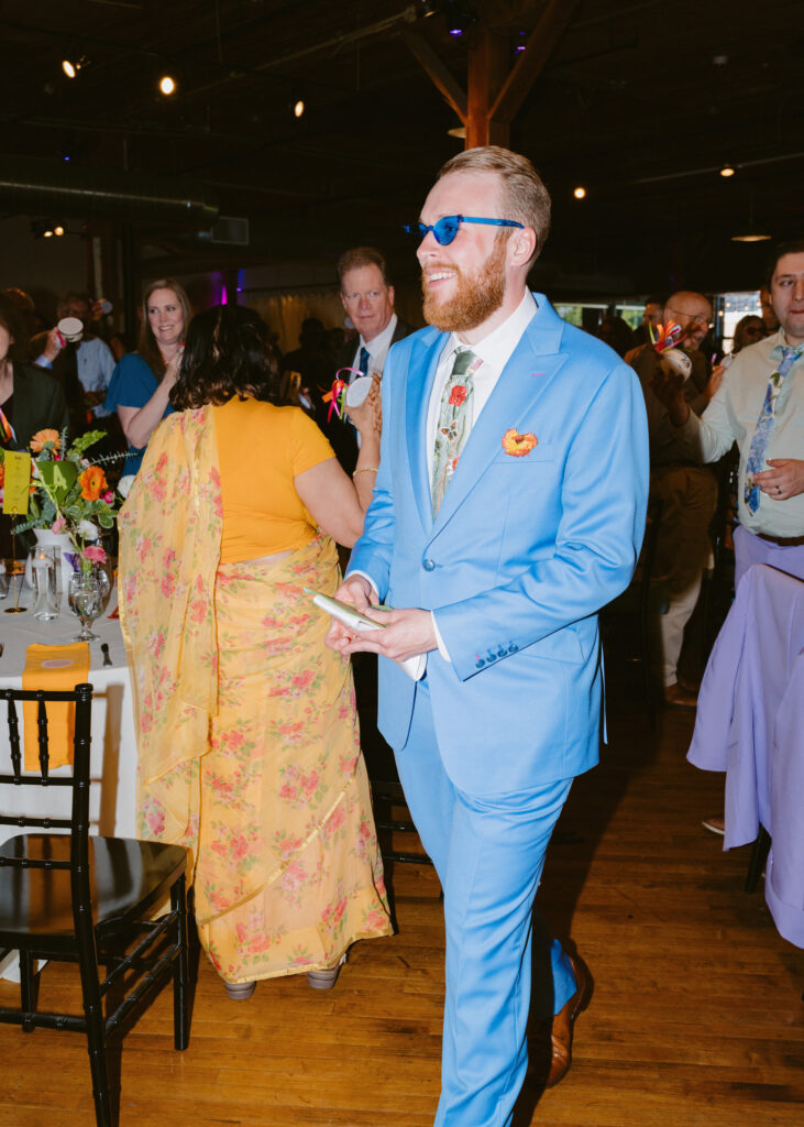 Groom smiles while wearing blue party sunglasses on the dance floor during the wedding reception.