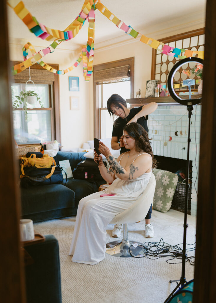 Bride smiles as she looks at her finished hairstyle in the mirror while getting ready on her wedding morning in Minneapolis, Minnesota.