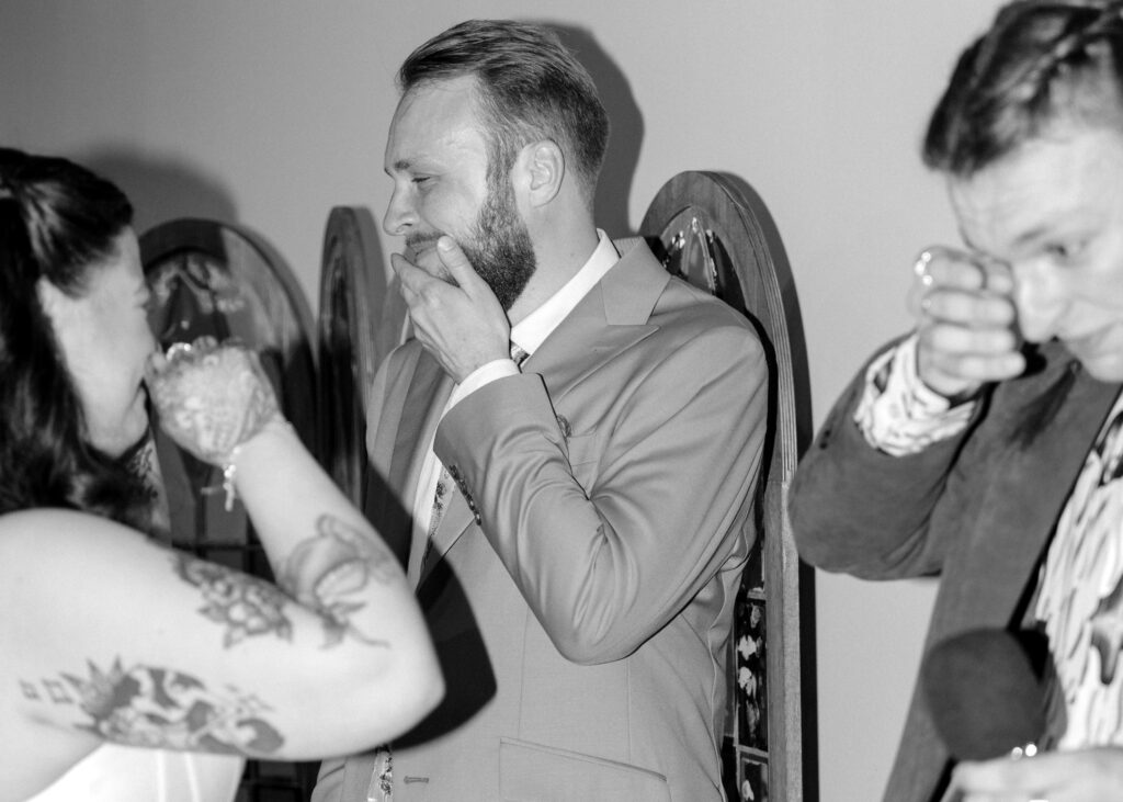 Bride and groom wipe away tears as they share an emotional moment with the groom’s brother during the wedding reception.