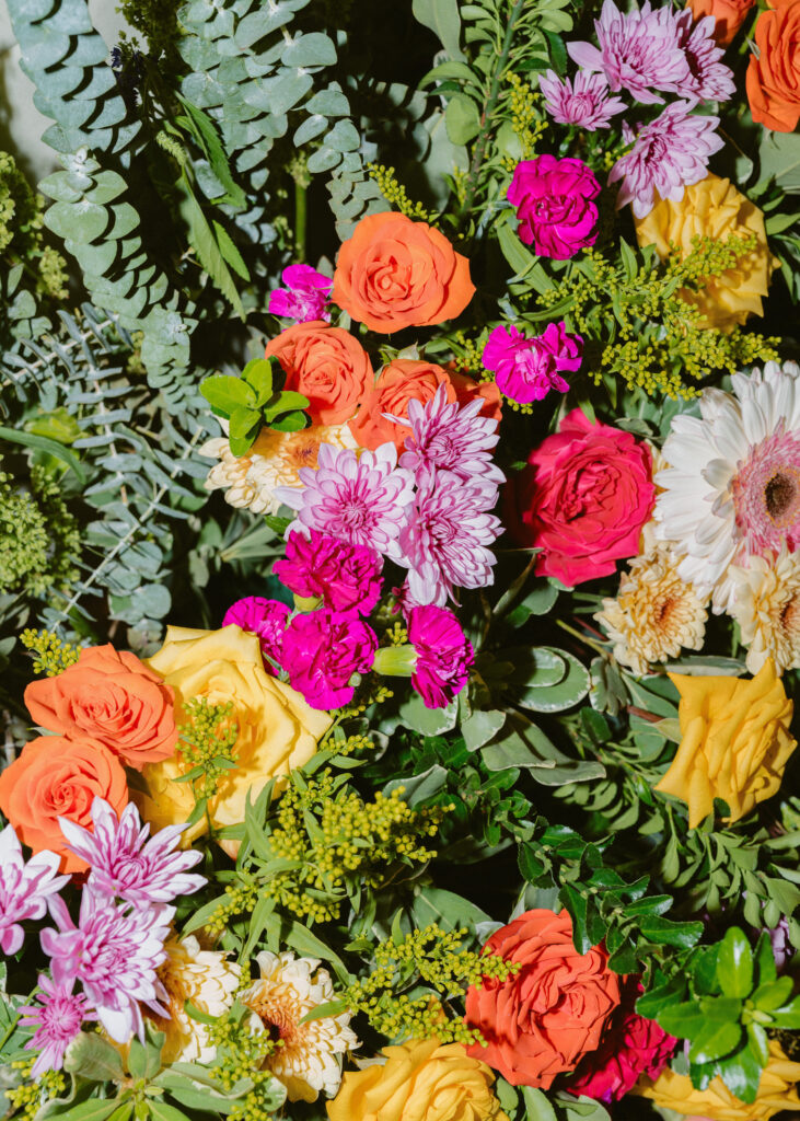 Colorful wedding floral arrangement featuring bright roses, chrysanthemums, eucalyptus, and greenery at the reception.
