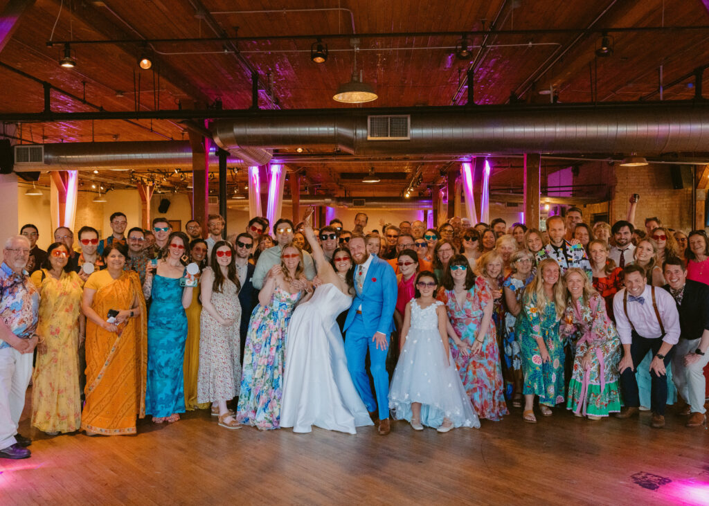 Bride and groom gather with wedding guests for a group portrait during their colorful reception at Solar Arts Building in Minneapolis.